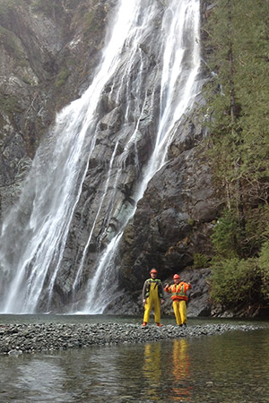 Two men in safety gear beside a waterfall